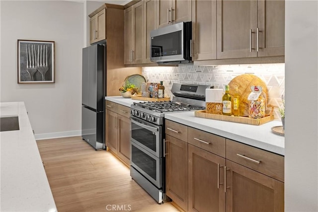 kitchen with tasteful backsplash, stainless steel appliances, and light hardwood / wood-style floors