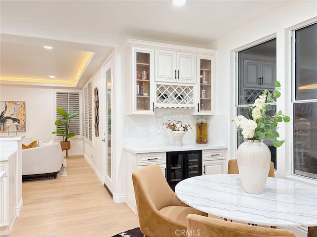 bar featuring a raised ceiling, wine cooler, tasteful backsplash, light hardwood / wood-style floors, and white cabinetry