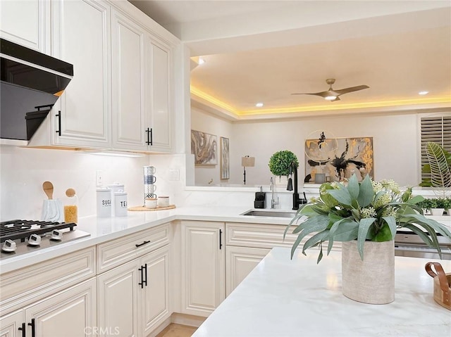 kitchen featuring white gas cooktop, a raised ceiling, ceiling fan, sink, and white cabinets