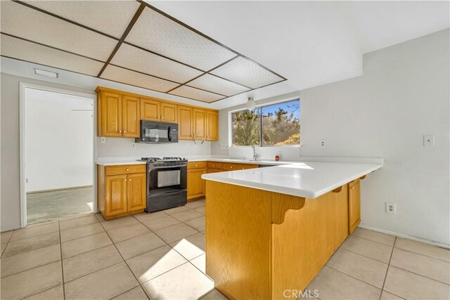 kitchen with black appliances, a paneled ceiling, light tile patterned flooring, and kitchen peninsula