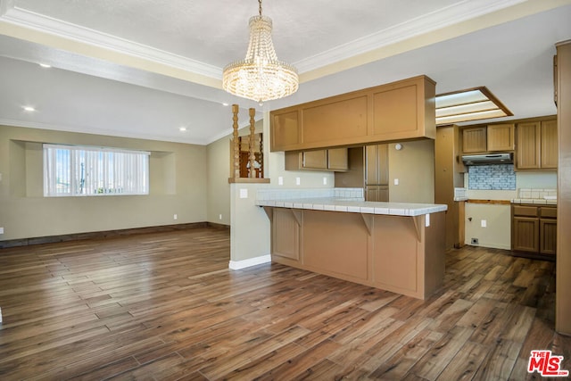 kitchen featuring dark wood-type flooring, an inviting chandelier, kitchen peninsula, tile countertops, and ornamental molding