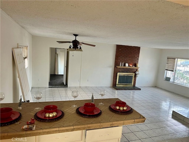 kitchen featuring a brick fireplace, a textured ceiling, ceiling fan, tile countertops, and light tile patterned flooring