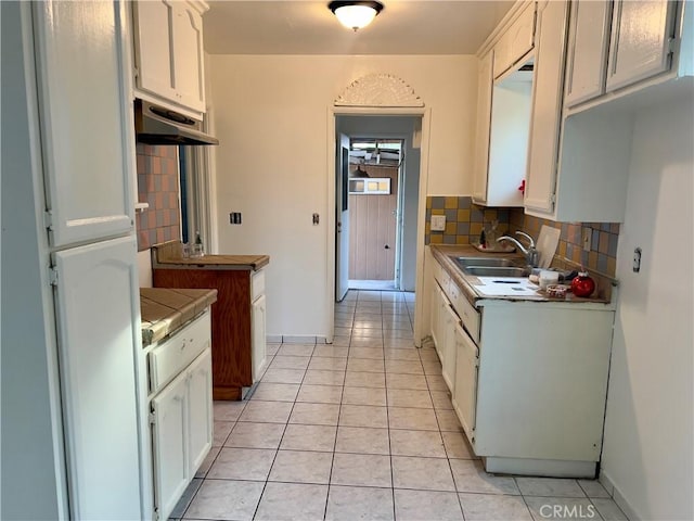 kitchen with light tile patterned floors, backsplash, white cabinetry, and sink