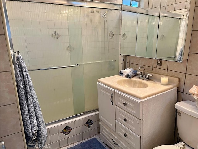 full bathroom with shower / bath combination with glass door, vanity, toilet, and tile walls