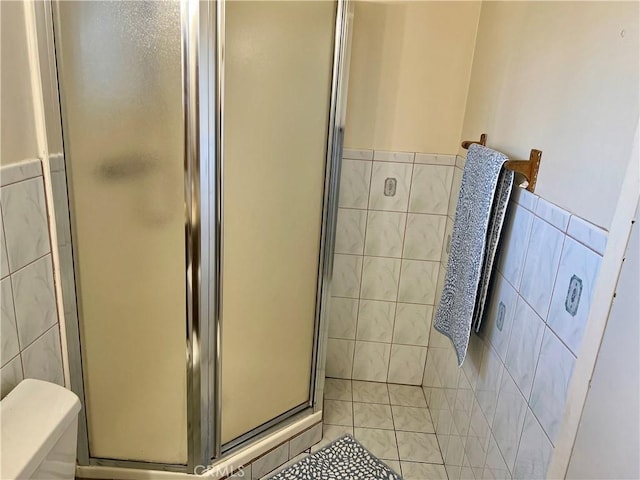 bathroom with tile patterned floors, toilet, tile walls, and walk in shower