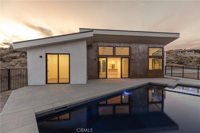 back house at dusk featuring a swimming pool with hot tub and a patio