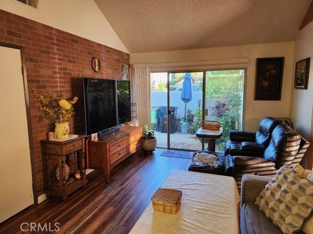 living room with dark hardwood / wood-style floors, lofted ceiling, a textured ceiling, and brick wall