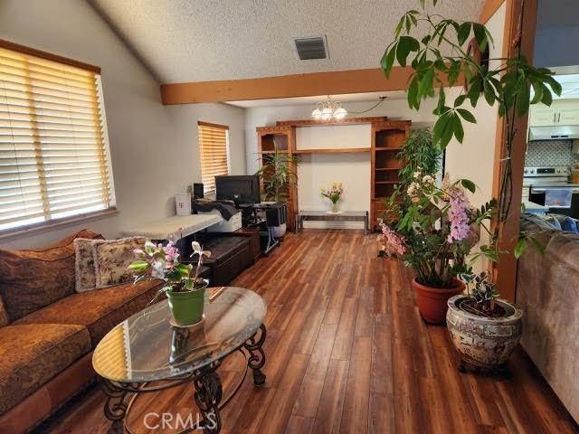 living room featuring a chandelier, dark hardwood / wood-style flooring, a textured ceiling, and vaulted ceiling