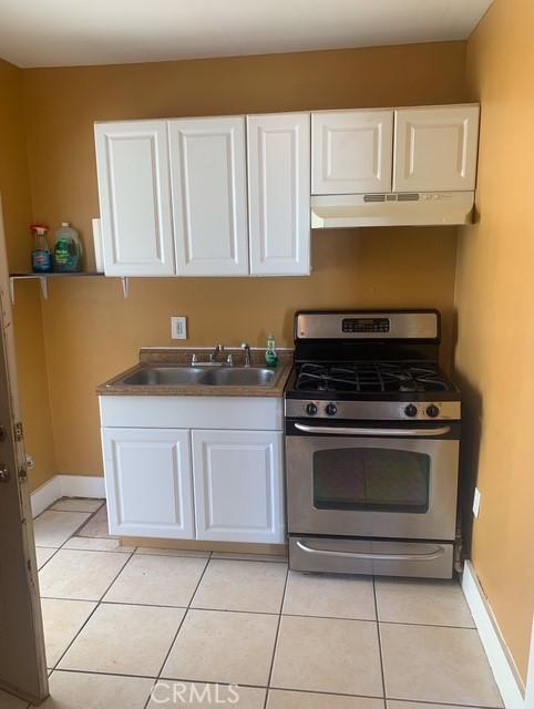 kitchen with light tile patterned floors, sink, stainless steel gas range, and white cabinetry