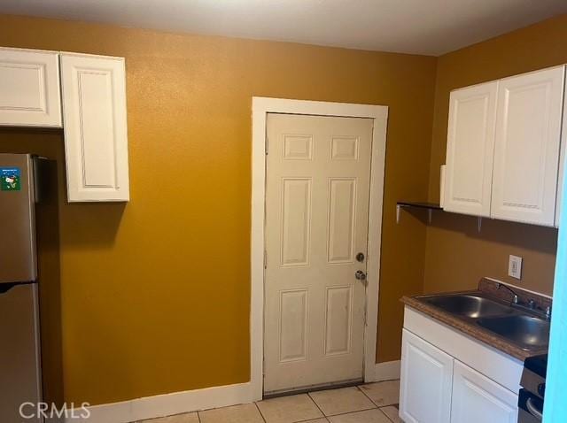 kitchen with light tile patterned floors, white cabinets, and stainless steel fridge