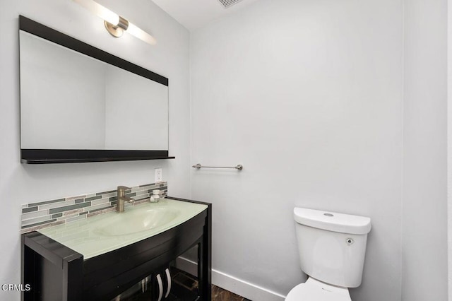 half bathroom featuring toilet, visible vents, vanity, baseboards, and tasteful backsplash