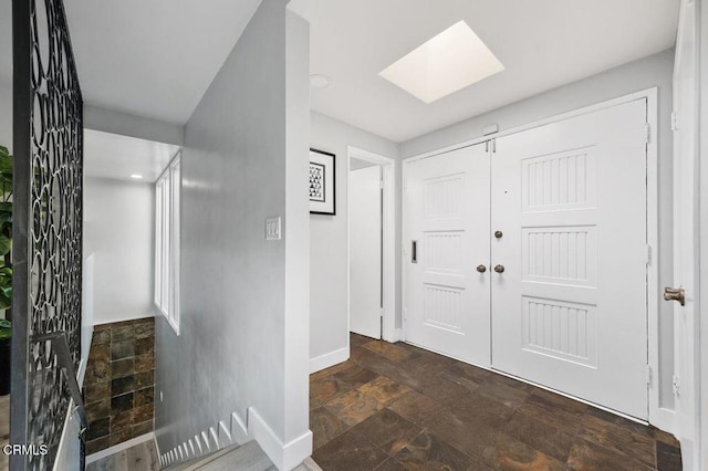 entrance foyer featuring a skylight, stone finish flooring, and baseboards