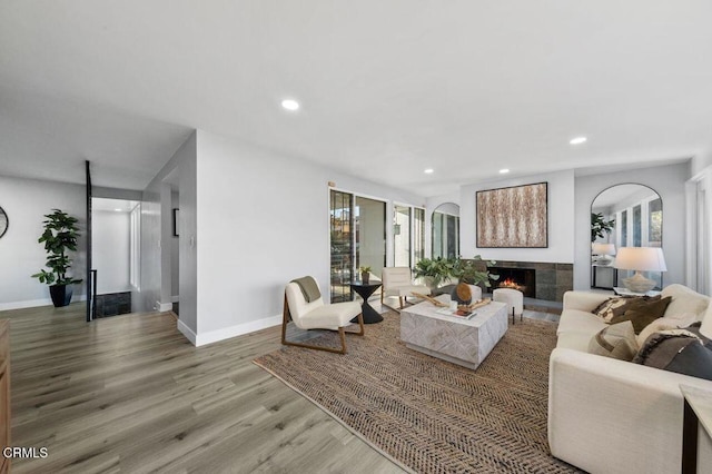 living area with recessed lighting, a lit fireplace, baseboards, and wood finished floors