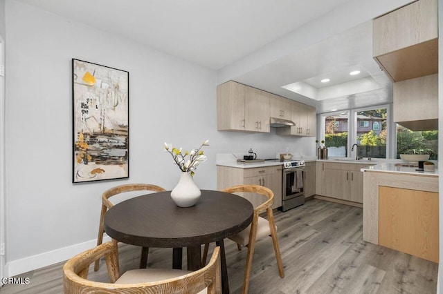 kitchen featuring under cabinet range hood, light countertops, stainless steel range with electric stovetop, light brown cabinets, and a sink