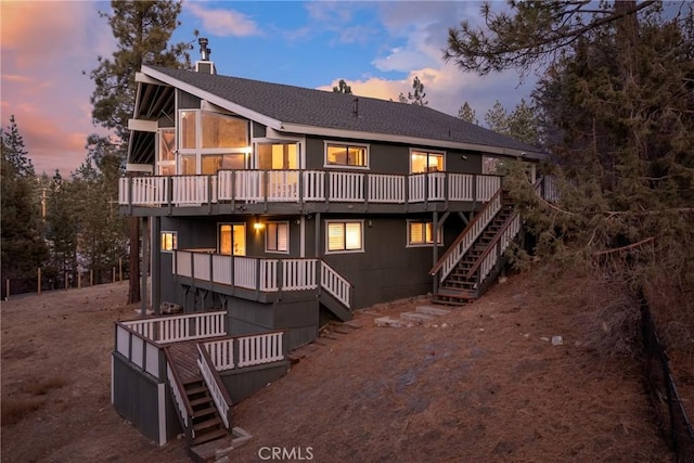 back house at dusk featuring a sunroom and a deck