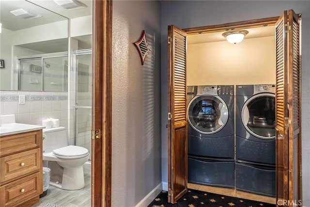 clothes washing area featuring light tile patterned flooring, independent washer and dryer, and tile walls