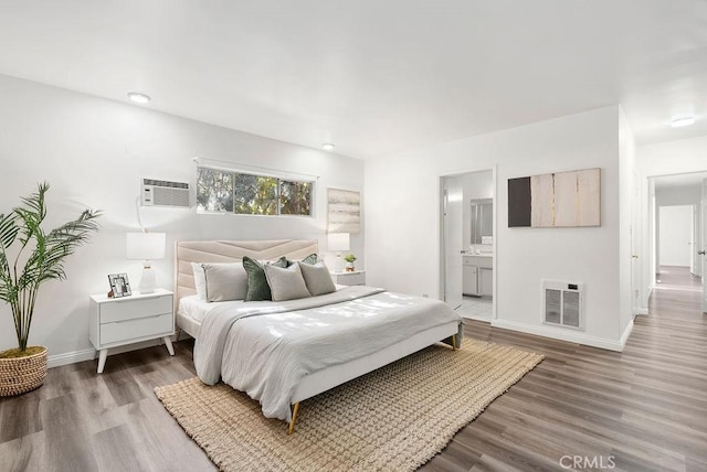 bedroom featuring hardwood / wood-style floors, heating unit, connected bathroom, and a wall mounted AC