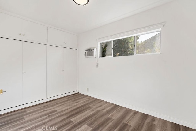 unfurnished bedroom featuring a wall unit AC, a closet, and hardwood / wood-style flooring