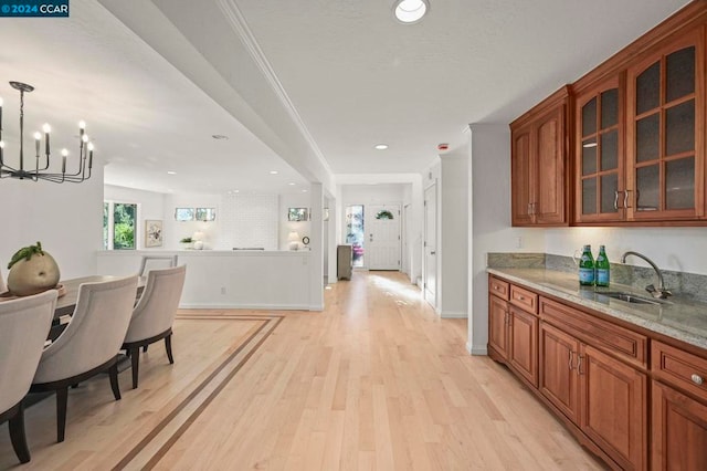 kitchen featuring decorative light fixtures, a chandelier, light hardwood / wood-style flooring, light stone counters, and sink