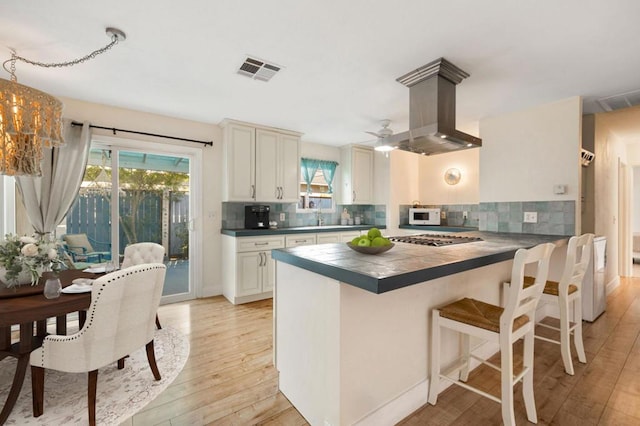 kitchen with tile countertops, kitchen peninsula, island exhaust hood, stainless steel gas stovetop, and backsplash