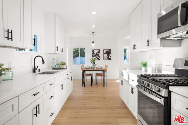 kitchen featuring pendant lighting, sink, light wood-type flooring, appliances with stainless steel finishes, and white cabinetry