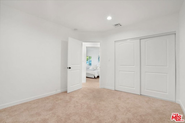 unfurnished bedroom with light carpet and a closet