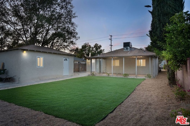 back house at dusk featuring central AC and a yard