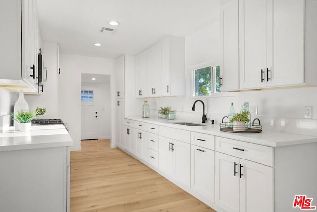 kitchen with light hardwood / wood-style floors, white cabinetry, and sink