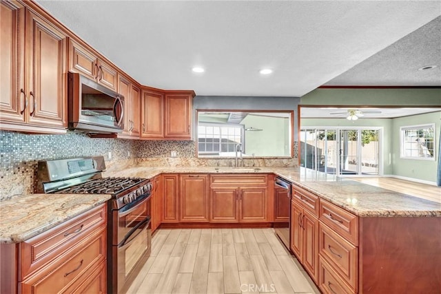 kitchen with sink, appliances with stainless steel finishes, light stone counters, light hardwood / wood-style floors, and decorative backsplash