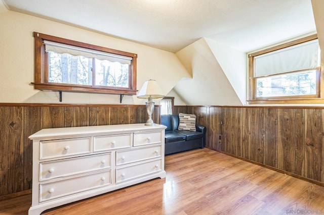 additional living space with wooden walls, light hardwood / wood-style floors, lofted ceiling, and a wealth of natural light