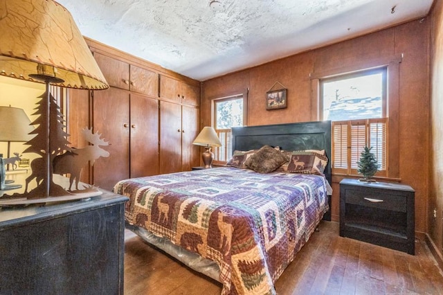 bedroom with a textured ceiling, dark hardwood / wood-style flooring, a closet, and wooden walls