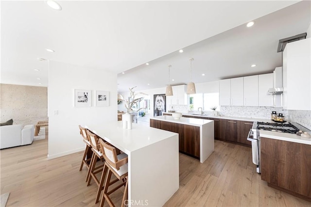 kitchen featuring a kitchen island, a breakfast bar, hanging light fixtures, white cabinets, and gas range