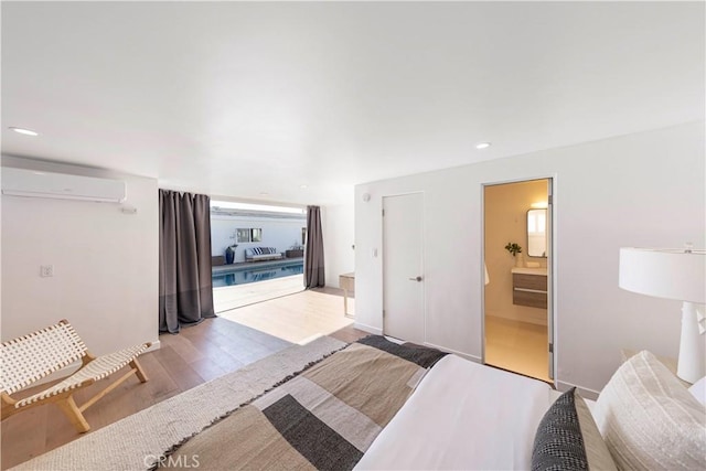 bedroom featuring light hardwood / wood-style floors, ensuite bath, and a wall mounted air conditioner