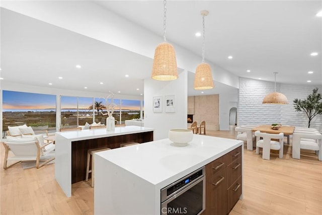 kitchen with hanging light fixtures, a center island, stainless steel oven, and light hardwood / wood-style flooring