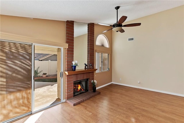 living room with baseboards, wood finished floors, vaulted ceiling, a textured ceiling, and a brick fireplace