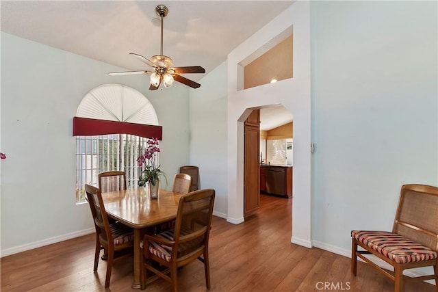 dining space with baseboards, arched walkways, ceiling fan, vaulted ceiling, and light wood-style floors