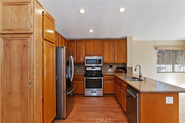 kitchen featuring light stone counters, a peninsula, a sink, appliances with stainless steel finishes, and light wood finished floors