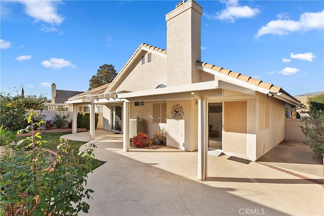 back of house featuring stucco siding, a chimney, fence, and a patio