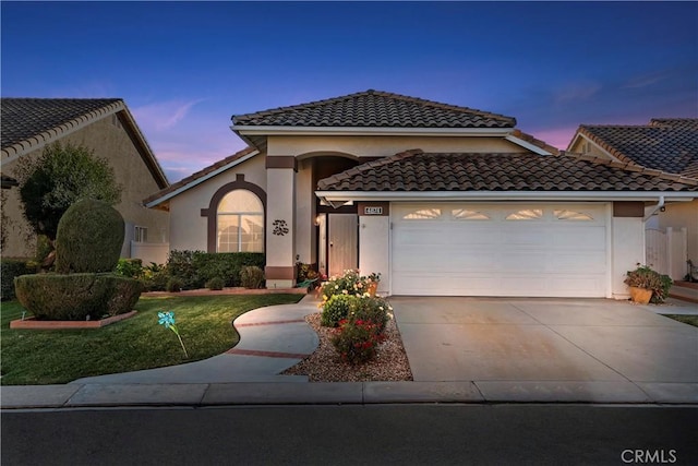 mediterranean / spanish-style home featuring driveway, a garage, stucco siding, a tile roof, and a front yard