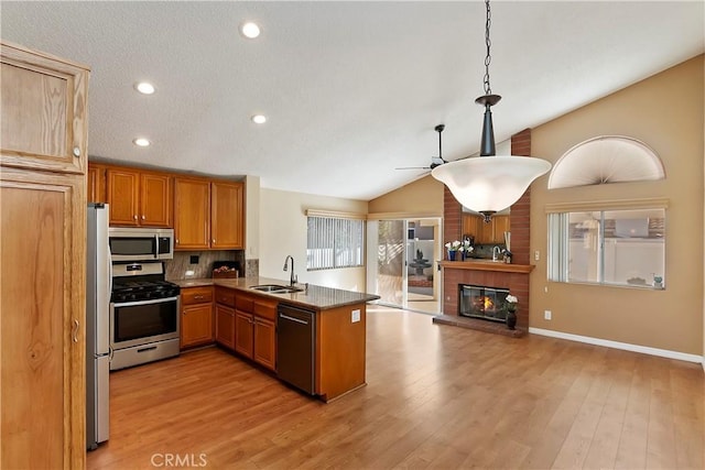 kitchen featuring stainless steel appliances, a brick fireplace, vaulted ceiling, plenty of natural light, and a peninsula