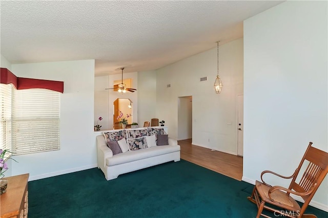 living area featuring baseboards, visible vents, a ceiling fan, a textured ceiling, and high vaulted ceiling