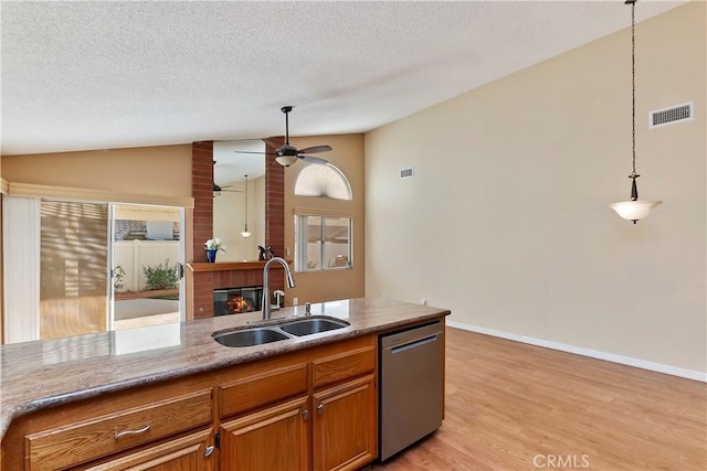 kitchen featuring a fireplace, a sink, vaulted ceiling, dishwasher, and brown cabinetry