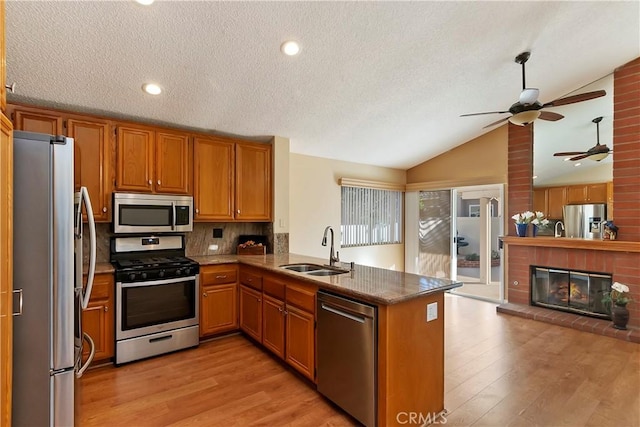 kitchen featuring a fireplace, stainless steel appliances, lofted ceiling, light wood-style floors, and a sink