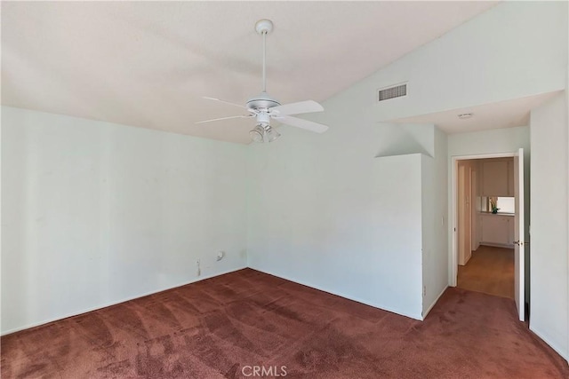 spare room featuring vaulted ceiling, visible vents, dark colored carpet, and a ceiling fan