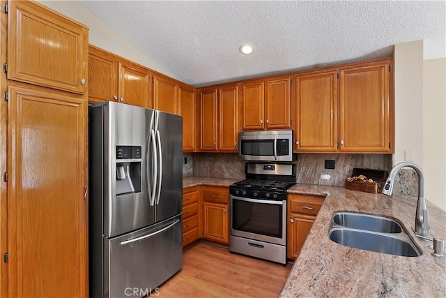 kitchen featuring light wood-style flooring, stainless steel appliances, a sink, decorative backsplash, and brown cabinetry