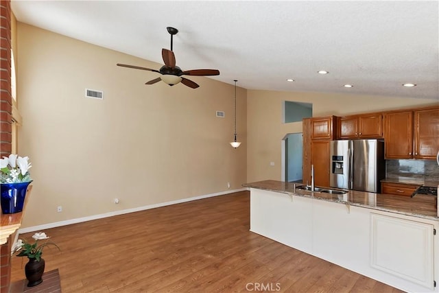 kitchen with brown cabinets, stainless steel refrigerator with ice dispenser, lofted ceiling, visible vents, and a sink