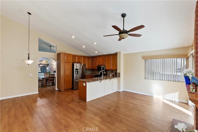 kitchen featuring stainless steel appliances, lofted ceiling, a sink, wood finished floors, and a peninsula