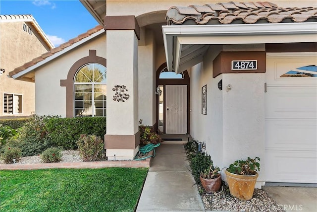 view of exterior entry featuring an attached garage, a tile roof, and stucco siding