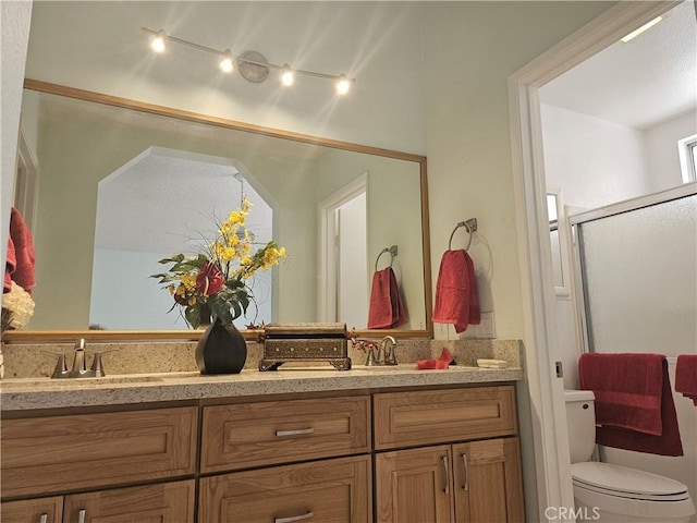 bathroom with double vanity, an enclosed shower, a sink, and toilet