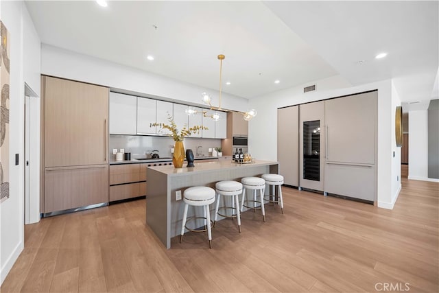 kitchen with pendant lighting, light wood-type flooring, a center island with sink, and white cabinetry